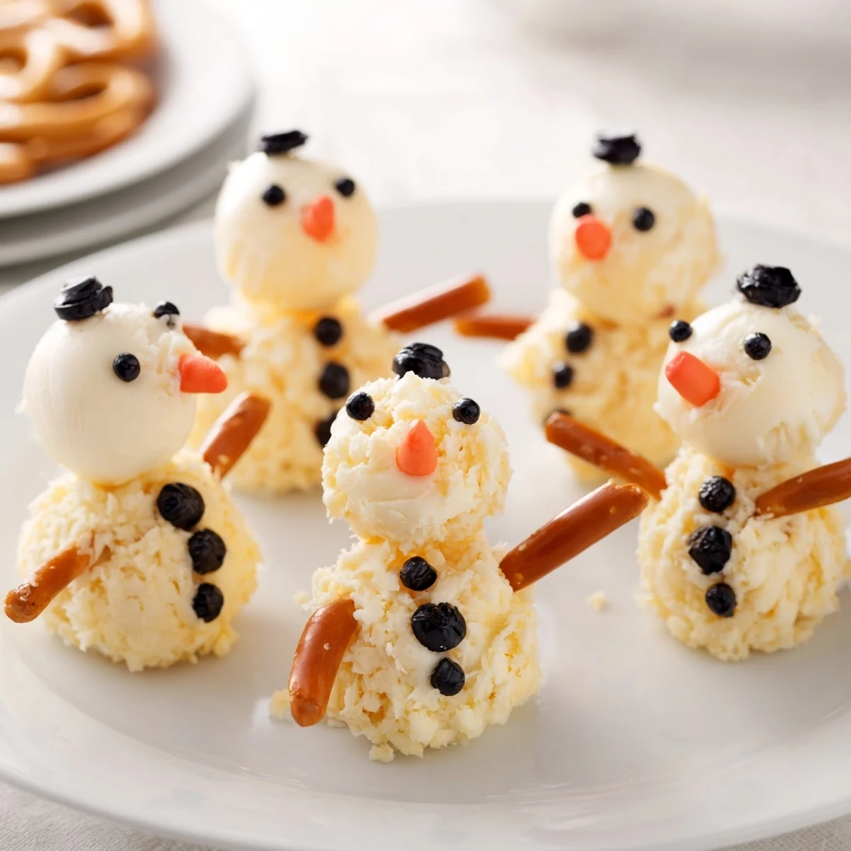 Melted Snowman Cheese Bites: Adorable, creamy cheese snowmen with black olive eyes and pretzel arms on a platter.