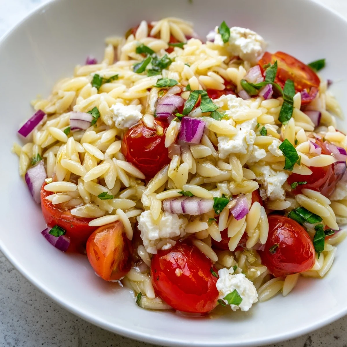 Brightly colored Tomato Feta Orzo pasta salad, featuring fresh tomatoes and crumbled feta cheese.
