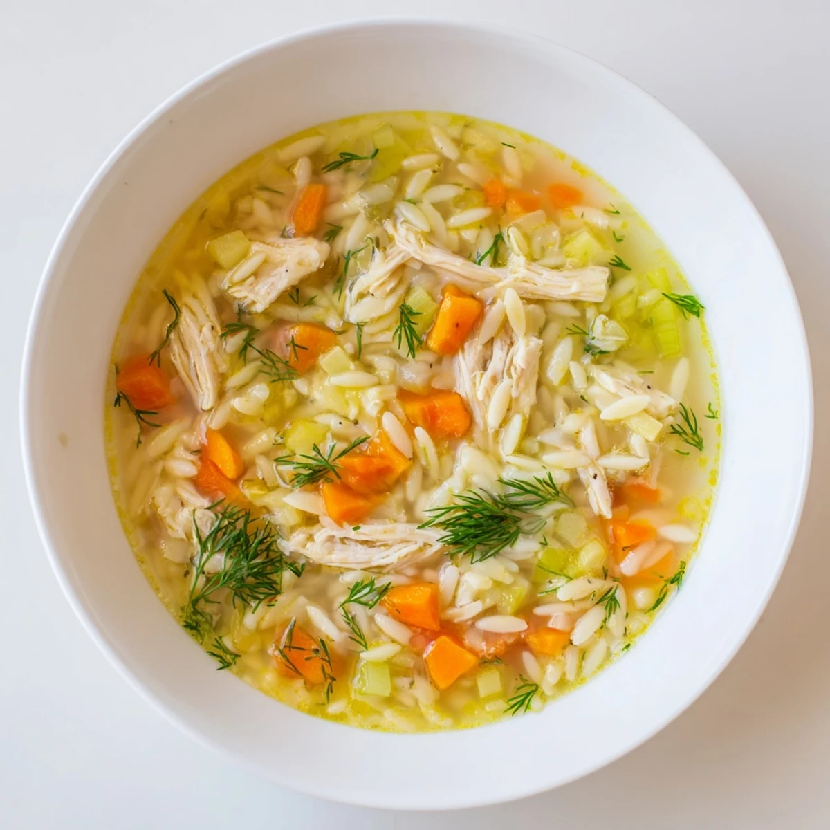 A bowl of Chicken Lemon Orzo Soup garnished with fresh dill, with tender chicken and orzo visible in the bright, brothy mixture.