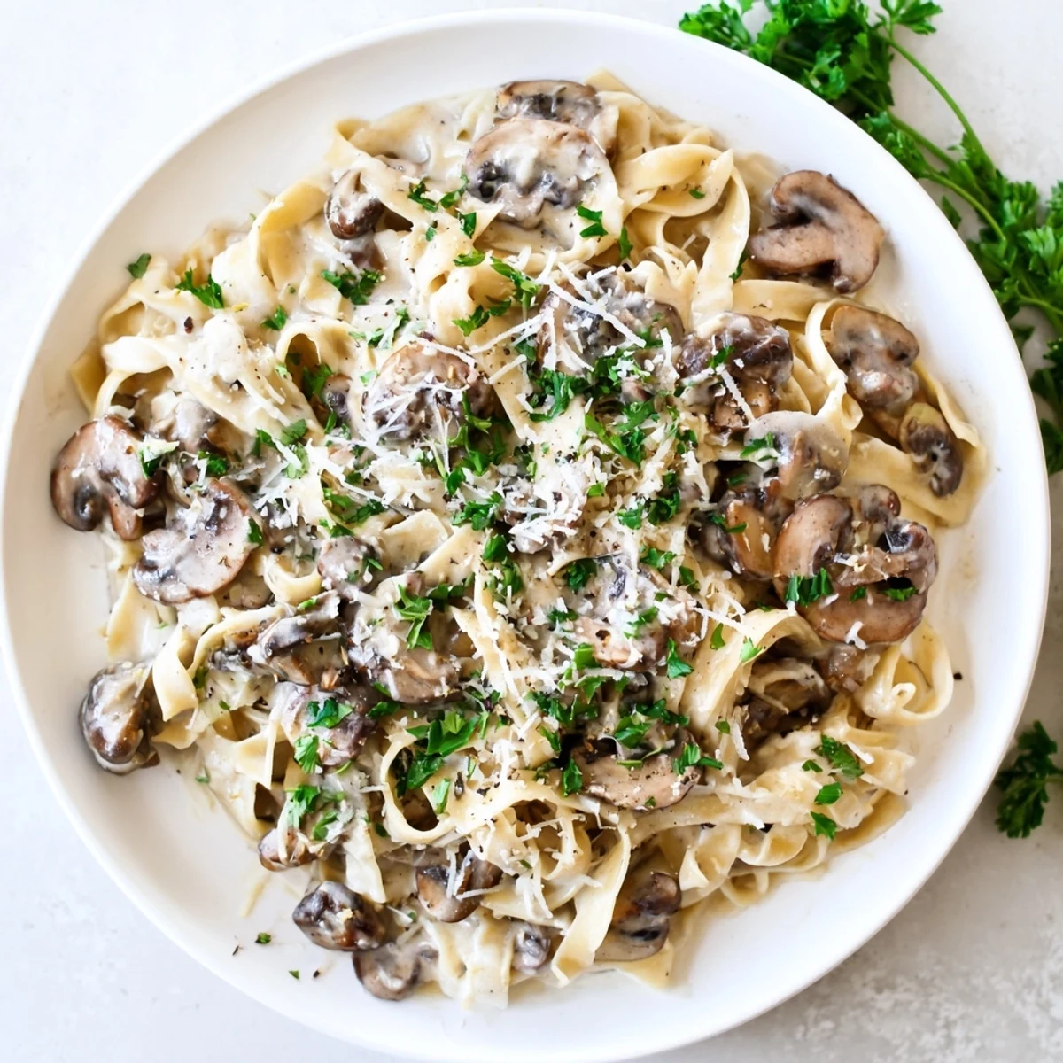 Creamy Mushroom Alfredo pasta swirls in a white bowl, garnished with fresh parsley and shaved Parmesan, steaming beside a wine glass.