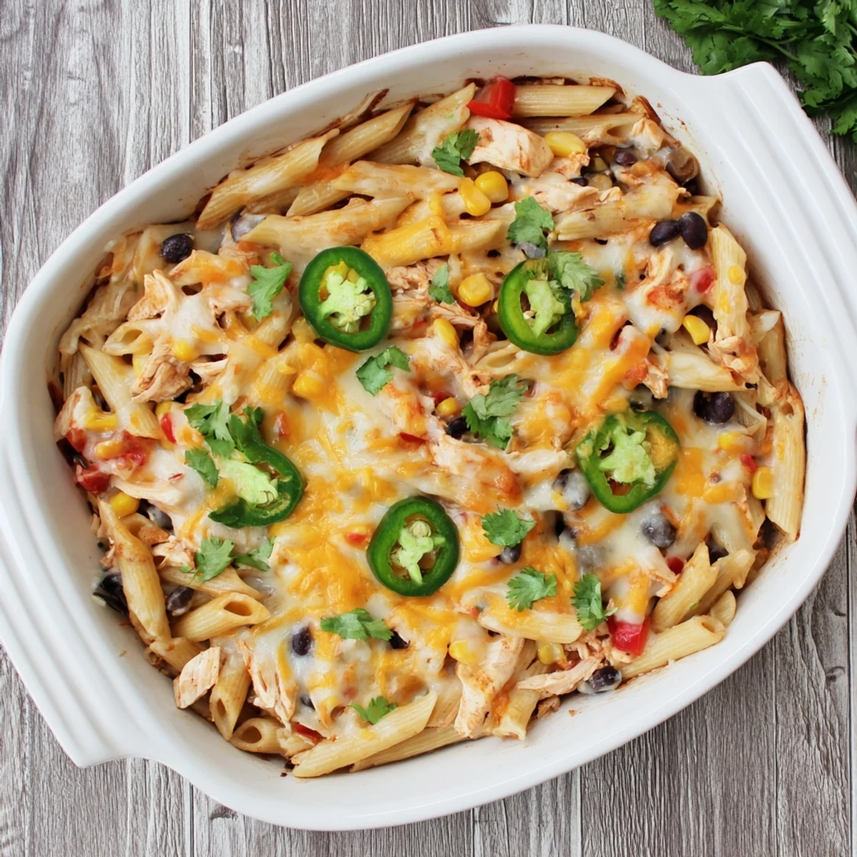 Serving of Chicken Burrito Pasta Bake on a white plate, garnished with fresh cilantro and a wedge of lime for a fresh finish.