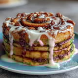 Decadent breakfast bake featuring cinnamon swirls in fluffy pancakes, topped with rich cream cheese glaze for extra indulgence.  