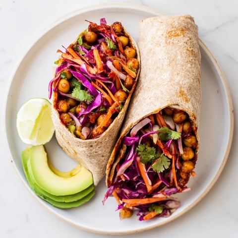 A close-up of a BBQ Chickpea & Slaw Wrap overflowing with colorful, crunchy slaw and delicious chickpeas.
