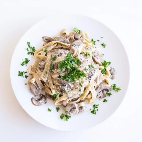 A skillet of Creamy Mushroom Alfredo shows sautéed golden mushrooms tossed in a luscious garlic parmesan cream sauce with fettuccine noodles.