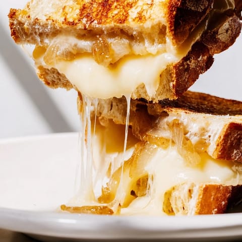 Two halves of a gourmet Caramelized Onion & Gruyère Grilled Cheese sandwich resting on a checkered napkin next to fresh thyme.