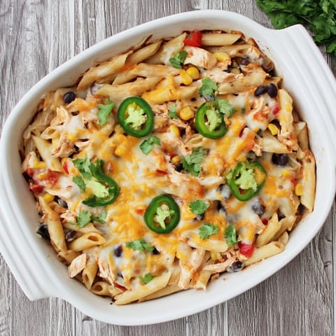 Serving of Chicken Burrito Pasta Bake on a white plate, garnished with fresh cilantro and a wedge of lime for a fresh finish.