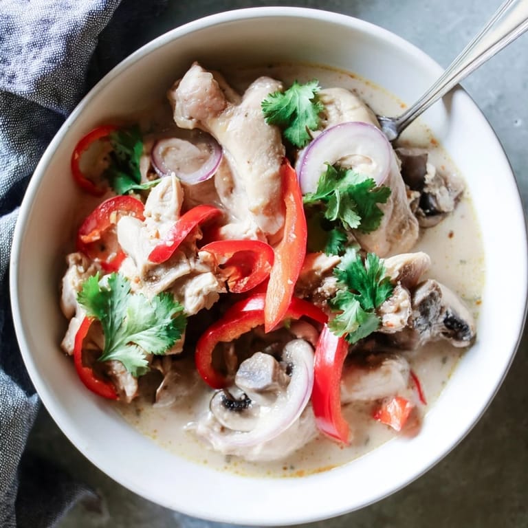 A creamy bowl of Crockpot Thai Coconut Chicken Soup garnished with fresh herbs and chilies.  
