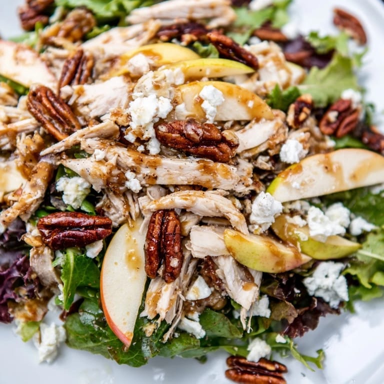 Crisp mixed greens and vibrant red onion mingle with juicy apple slices and savory chicken in this autumn salad, garnished with golden candied pecans.