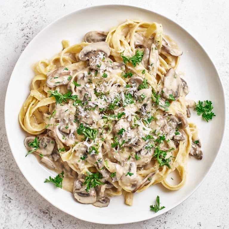 Close-up of Creamy Mushroom Alfredo, the velvety white sauce clinging to silky pasta, flecked with herbs and rich mushrooms on a wooden table.
